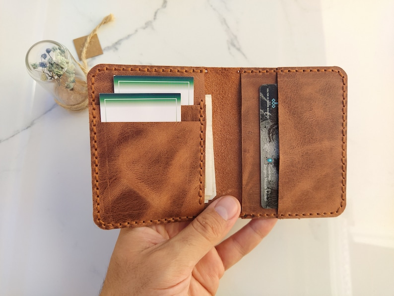 May include: A brown leather wallet with a stitched edge, open to reveal two card slots and a larger pocket for bills. The wallet has a worn, distressed look.