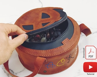 May include: A round brown leather bag with a zip fastening and a black interior. The bag has a stitched design on the front and a strap. The bag is open and filled with colourful stones.