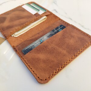 May include: A brown leather wallet with multiple card slots and a billfold. The wallet is open and shows a credit card and some bills inside.