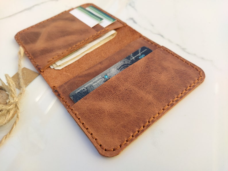 May include: A brown leather wallet with multiple card slots and a billfold. The wallet is open and shows a credit card and some bills inside.