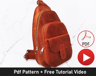 Peut inclure: Un sac à bandoulière en cuir marron avec une poche zippée et une poche à rabat. Le sac est sur un fond de marbre blanc. L'image comprend également une icône PDF et une icône de lecture, indiquant qu'un patron et une vidéo de tutoriel sont disponibles.