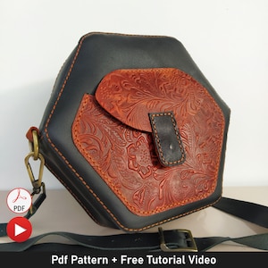 Könnte beinhalten: Eine sechseckige Leder-Umhängetasche mit Klappenverschluss. Die Tasche ist schwarz mit einer braunen, floral geprägten Ledertasche auf der Vorderseite. Die Tasche hat einen Riemen und einen Metallverschluss.