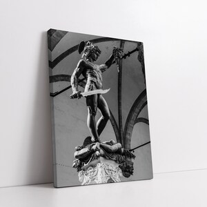 May include: Black and white photograph of a statue of a man holding a sword and a severed head. The statue is standing on a pedestal with a base.