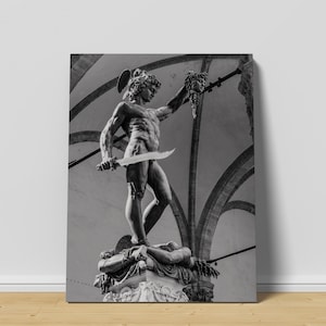 May include: Black and white photograph of a statue of a man holding a sword and the severed head of a woman. The statue is in a public square with arches in the background.
