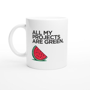 Puede incluir: Taza de cerámica blanca con el texto "ALL MY PROJECTS ARE GREEN." Una ilustración de una rodaja de sandía está debajo del texto. La taza tiene un asa curva y está sobre un fondo blanco.