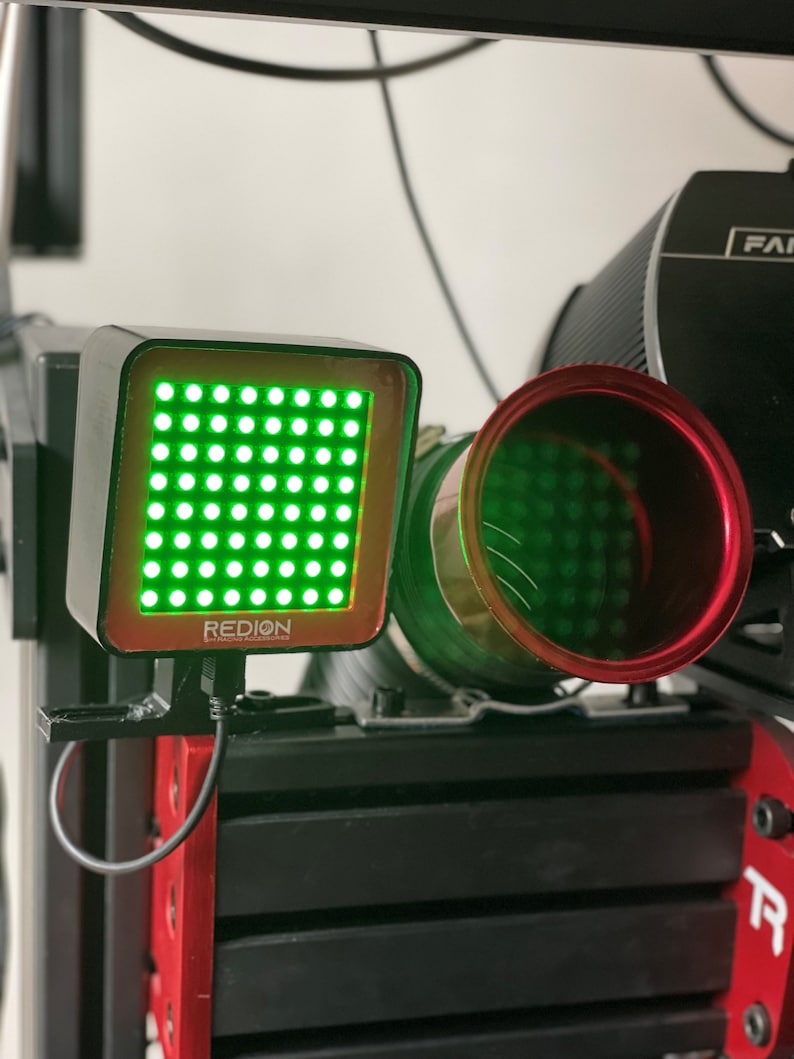 May include: A black and red electronic device with the word "REDION" printed on it. The device has a grid of green lights and is connected to a black cable. A red and green cylindrical component is also visible.