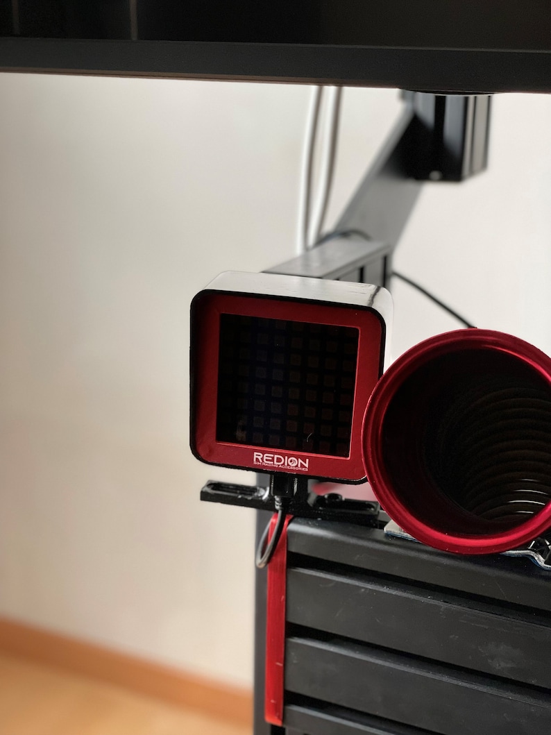 May include: A black and red device with the word "REDION" printed on it. The device has a red square screen and is attached to a black structure. A red cylindrical object is next to the device.
