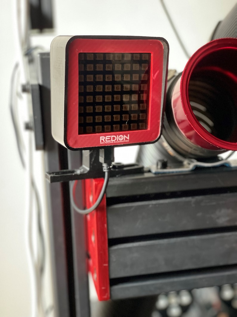 May include: A red and black electronic device with the text "REDION" on the front. The device has a grid of small squares on the front and is mounted on a black frame. A red circular component is visible on the right.