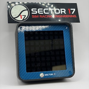 May include: A black and blue electronic device with a screen, featuring the text "SECTOR 17 SIM RACING ENGINEERING." The device has a carbon fiber texture on the edges and the logo "SECTOR 7" at the bottom. The screen displays a grid pattern.