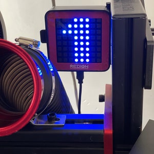 May include: A black and red digital display with the number 1 illuminated in blue. The display is mounted on a black frame with a red accent. The word "REDION" is printed on the display.