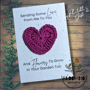 May include: A white card with the text "Sending Some Love From Me To You" and "And Flowers To Grow In Your Garden Too." A crocheted magenta heart is affixed to the card. The card is a plantable gift.