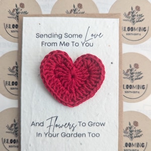 May include: A handmade greeting card with a red crocheted heart. The card reads "Sending Some Love From Me To You" and "And Flowers To Grow In Your Garden Too". The background includes circular stickers with floral designs.