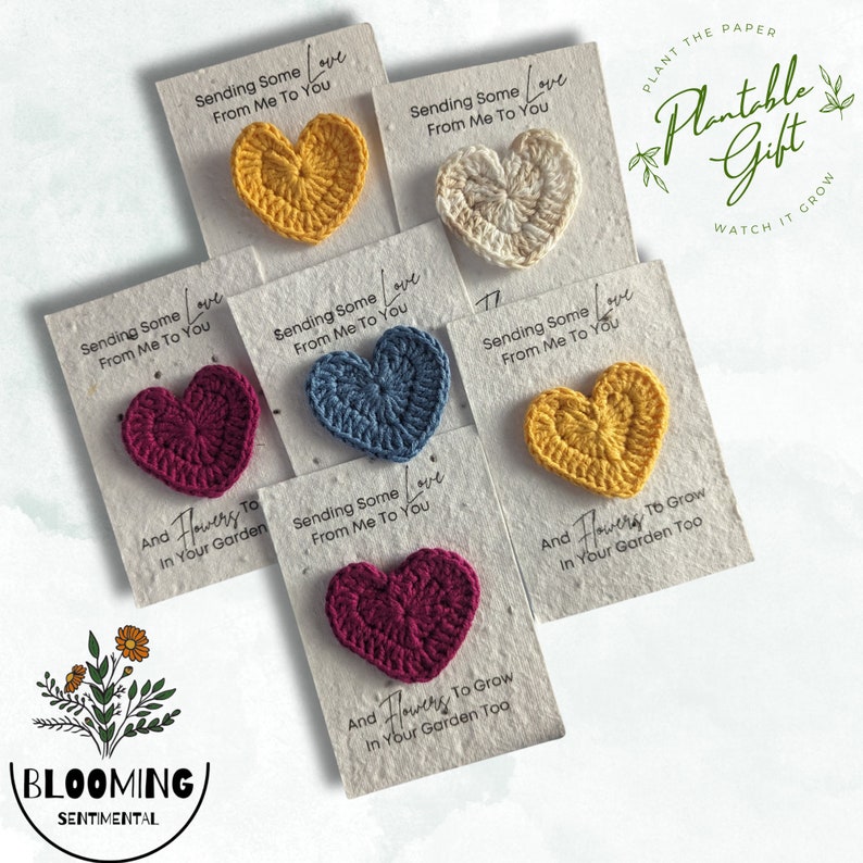 May include: A collection of handmade crochet heart gifts in various colors, including yellow, white, blue, and burgundy, attached to cards. The cards read "Sending Some Love From Me To You" and "And Flowers To Grow In Your Garden Too."