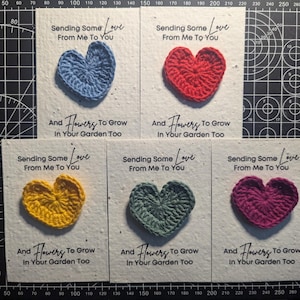 May include: A collection of handmade greeting cards, each featuring a crocheted heart in various colors: blue, red, yellow, green, and purple. The cards have the text "Sending Some Love From Me To You" and "And Flowers To Grow In Your Garden Too."