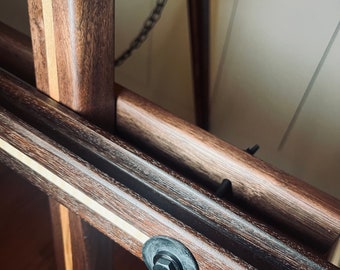 May include: Close-up of a wooden easel with a black metal chain and a black metal bolt with a rubber washer. The wood is a dark brown with light brown stripes.
