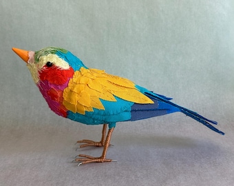 May include: A decorative bird ornament in bright colours. The bird has a blue body, yellow wings, and a red breast. The head is green and white, with an orange beak. It has wire legs and a long blue tail.