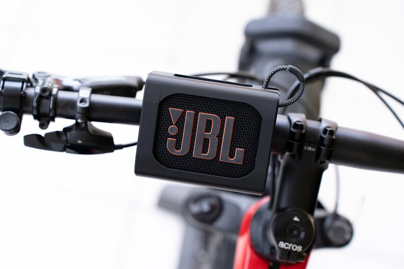 K&ouml;nnte beinhalten: Ein schwarzer JBL-Tragbarer Lautsprecher, der an den Lenker eines Fahrrads montiert ist.