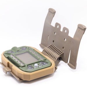 May include: A green and tan wildlife camera with a digital display and a variety of buttons. The camera is attached to a tan mounting bracket.