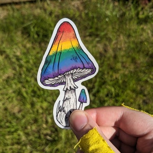 May include: A rainbow-coloured mushroom sticker with a white outline. The mushroom has a white stem and a small, purple mushroom growing from the side.