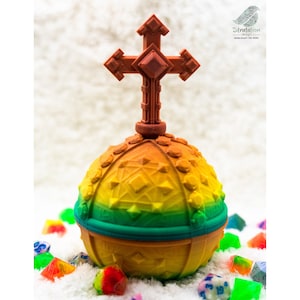 May include: A multi-colored, spherical object with a cross on top, surrounded by colorful dice. The sphere transitions from yellow to green, with orange accents. The cross is brown. The object is on a white, fluffy surface.