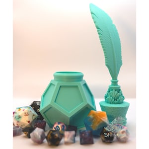 May include: A teal-colored inkwell, quill, and dice set. The inkwell has a geometric design, and the quill is shaped like a feather. Various polyhedral dice in different colors and patterns are scattered around the inkwell. The image has a soft, diffused lighting.