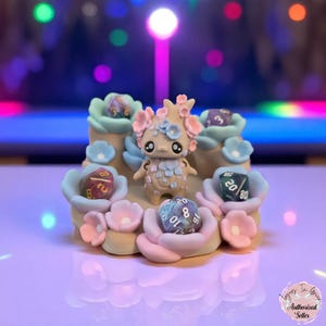 May include: A whimsical, handcrafted figurine featuring a small creature with floral accents, surrounded by pastel-colored flowers and dice. The figurine is a unique decorative item, perfect for tabletop gaming enthusiasts.