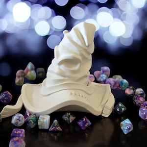 May include: A white ceramic Sorting Hat from the Harry Potter series, with a brim that is open and tipped to the side. The hat is surrounded by colorful, multi-sided dice.