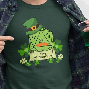 May include: A green t-shirt with a green 20-sided die with a leprechaun hat on top. The die has the numbers 2, 8, 20, 14, and 3 on it. The shirt also has the text "Happy St. Patrick's Day" on it.
