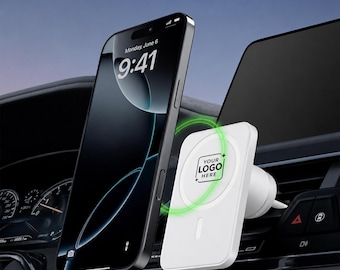 Peut inclure: Un support de téléphone magnétique blanc pour voiture fixé à une grille d'aération, doté d'une face carrée avec le texte YOUR LOGO HERE et un indicateur de charge circulaire vert, à côté d'un smartphone noir affichant une horloge numérique.
