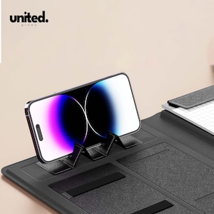 May include: A black phone stand with a smartphone resting on it. The phone displays a colorful screen. The stand has a textured surface and the word "united." is printed in the upper left corner.