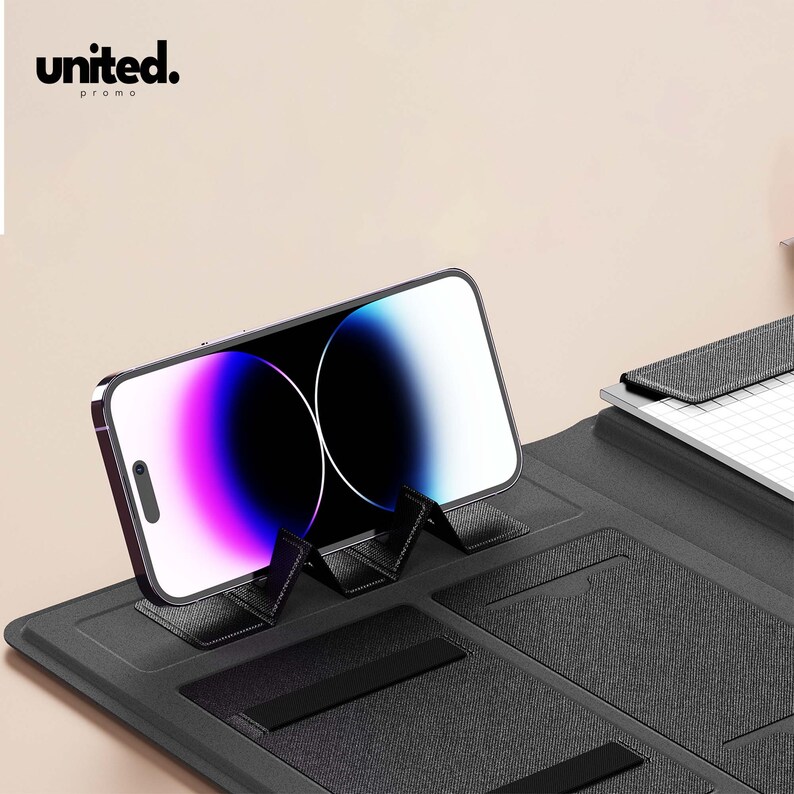 May include: A black phone stand with a smartphone resting on it. The phone displays a colorful screen. The stand has a textured surface and the word "united." is printed in the upper left corner.