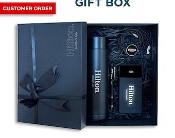 Könnte beinhalten: Eine schwarze Geschenkbox mit schwarzem Band, die eine schwarze Wasserflasche, einen Stift und eine Powerbank enthält, alle mit dem Logo "Hilton Santa Clara" versehen. Die Box enthält auch ein Ladekabel. Der Text "Personalized Corporate GIFT BOX" ist sichtbar.