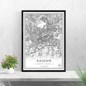 Könnte beinhalten: Schwarz-weiß gerahmter Kartendruck von Saigon, Vietnam. Die Karte zeigt die Straßen und Wasserwege der Stadt. Der Text "SAIGON" ist unten zentriert, mit Koordinaten und "VIETNAM" darunter. Eine Windrose befindet sich in der unteren rechten Ecke.