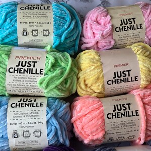 May include: A collection of Premier Just Chenille yarn skeins in various pastel colors, including blue, pink, green, and yellow. Each skein is labeled with text for crafters, knitters, and crocheters. The yarn is 65 yards/60 meters and made of 100% polyester.