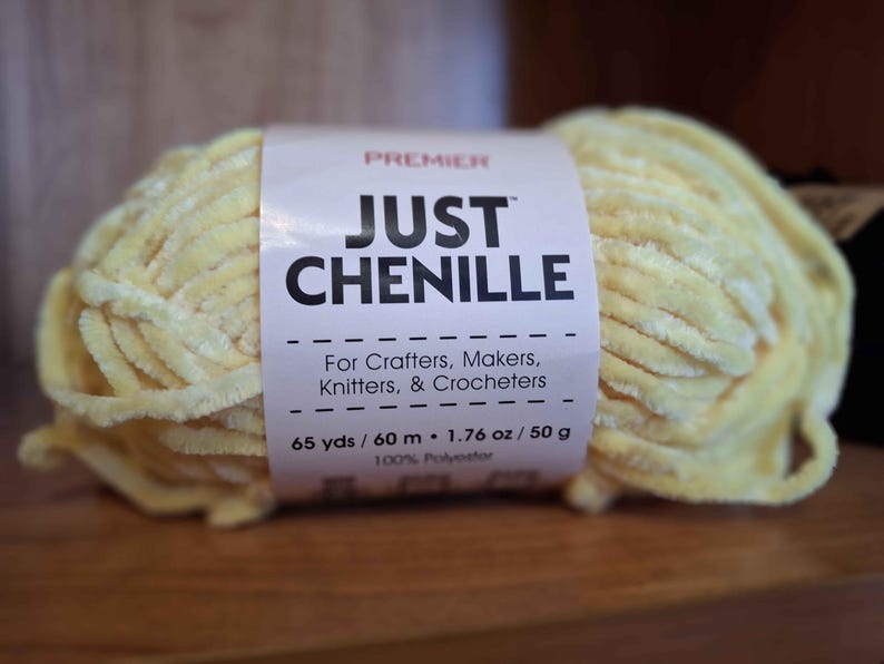May include: A skein of Premier Just Chenille yarn in a soft yellow color. The label reads "For Crafters, Makers, Knitters, & Crocheters." The yarn is 65 yards / 60 meters and 1.76 oz / 50 g of 100% polyester.