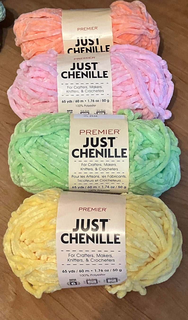 May include: Four skeins of Premier Just Chenille yarn in pastel colors: peach, pink, green, and yellow. Each skein is labeled with the text "For Crafters, Makers, Knitters, & Crocheters". The yarn is 65 yards / 60 meters and 1.76 oz / 50 g.