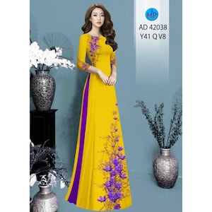 Könnte beinhalten: Ein gelbes Maxikleid mit einem violetten Blumendruck und einer violetten Seitenleiste. Das Kleid hat einen runden Ausschnitt und Dreiviertelärmel.