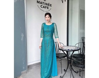 May include: A woman wearing a teal blue sequined maxi dress with a side slit. The dress has a round neckline and three-quarter sleeves. She is standing in front of a cafe with a sign that reads "Matinée Cafe" in black lettering.