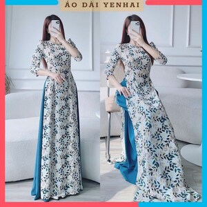 May include: A white dress with a teal blue underskirt and a leaf pattern. The dress has a high neckline and three-quarter sleeves. The dress is called "Áo Dài Yenhai".