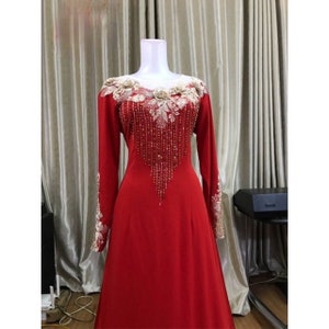 May include: A long-sleeved red dress with a beaded and lace neckline. The dress has a flowing skirt and is perfect for a special occasion.