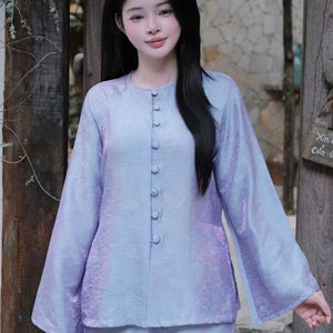 Può includere: Un top a maniche lunghe color viola chiaro con scollo rotondo e una fila verticale di bottoni rivestiti in tessuto abbinato sul davanti. Il capo presenta un sottile motivo jacquard tono su tono e maniche ampie e larghe.
