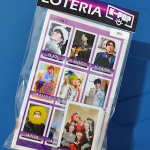 May include: A clear plastic package containing a set of cards. The cards feature images of a K-Pop group, with text in Spanish such as "EL SOL" and "EL CORAZON". The package is labeled "LOTERIA K-POP".