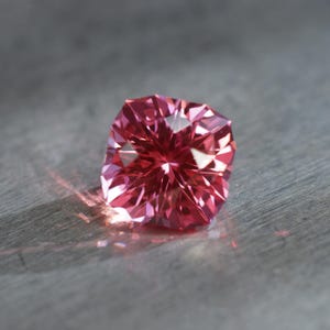 Peut inclure: Une pierre pr&eacute;cieuse rose &agrave; facettes, refl&eacute;tant la lumi&egrave;re sur une surface grise.