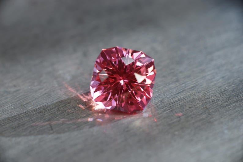 Peut inclure: Une pierre pr&eacute;cieuse rose &agrave; facettes, refl&eacute;tant la lumi&egrave;re sur une surface grise.
