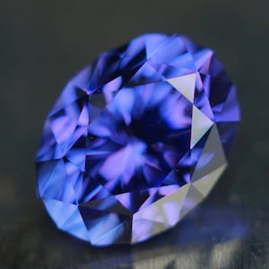 May include: A deep purple gemstone with a faceted cut. The gem has a starburst pattern in the center.