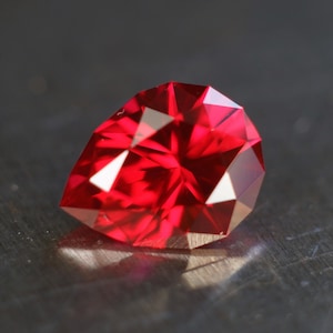 May include: A deep red pear-shaped gemstone with a faceted cut.