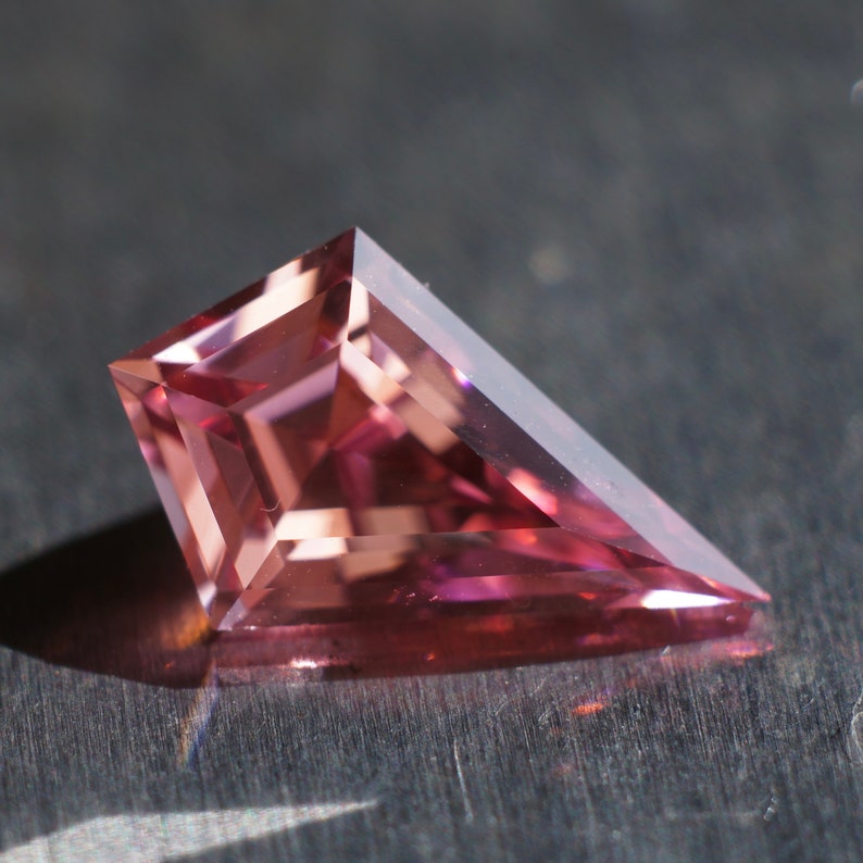May include: A pink, faceted gemstone with a triangular shape.