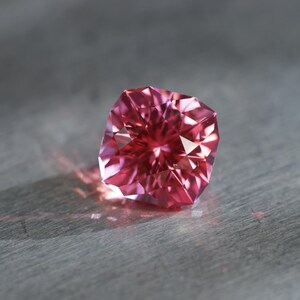 Peut inclure: Une pierre pr&eacute;cieuse rose avec une taille facet&eacute;e, refl&eacute;tant la lumi&egrave;re.