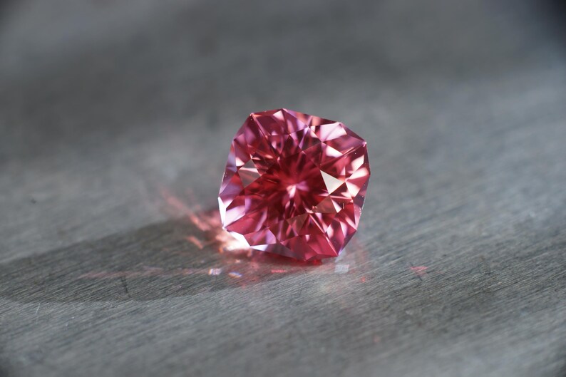 Peut inclure: Une pierre pr&eacute;cieuse rose avec une taille facet&eacute;e, refl&eacute;tant la lumi&egrave;re.