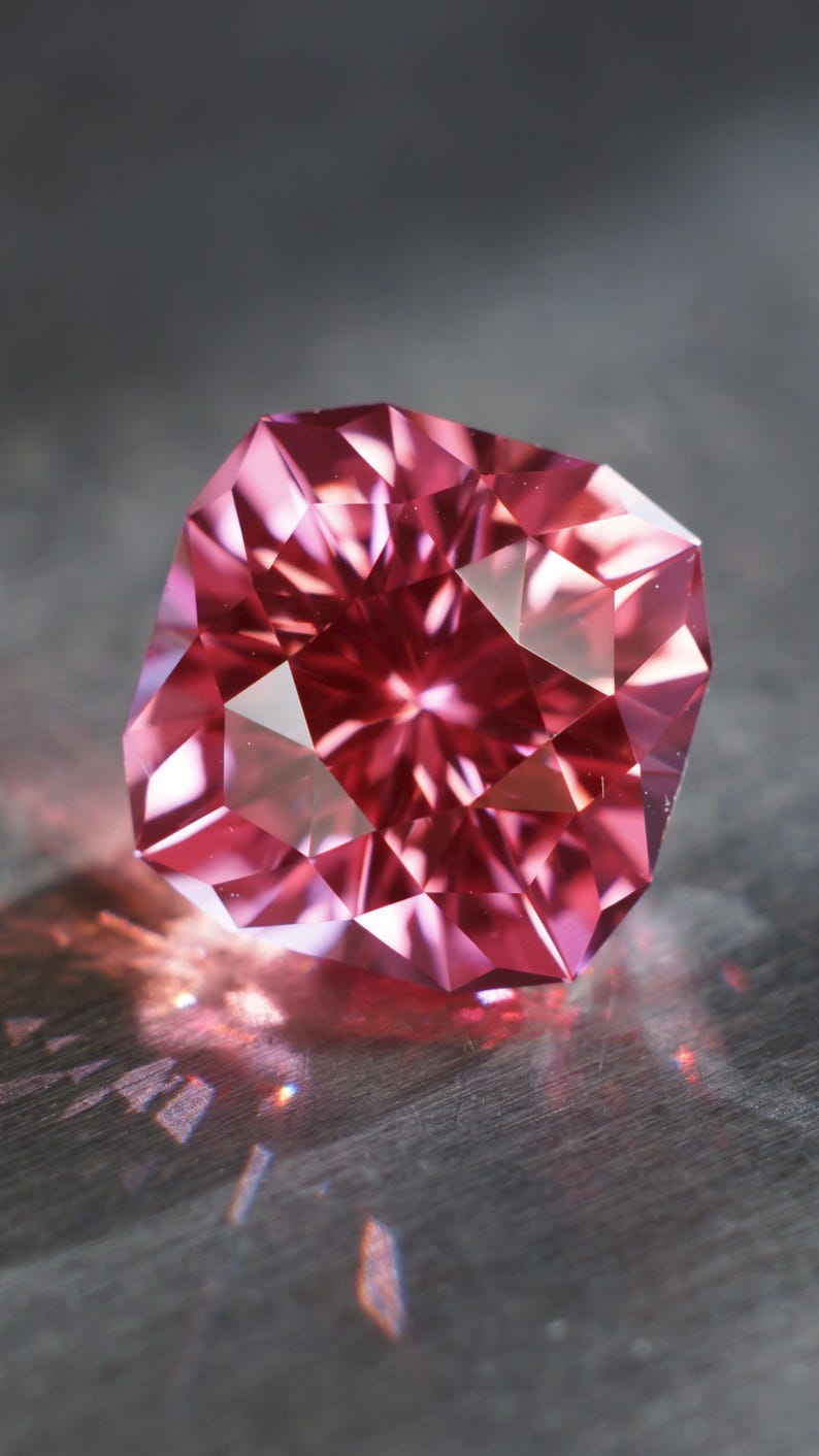 Peut inclure: Une pierre pr&eacute;cieuse rose &agrave; facettes, refl&eacute;tant la lumi&egrave;re sur une surface grise.